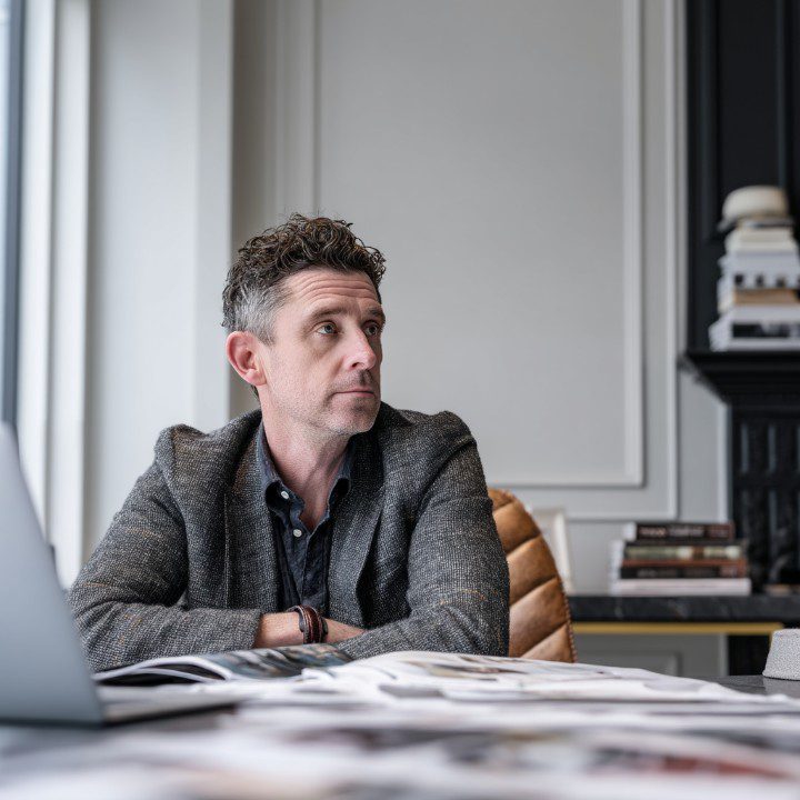 A thoughtful CEO in his late forties sits in a modern office with documents and a laptop, reflecting on business planning.