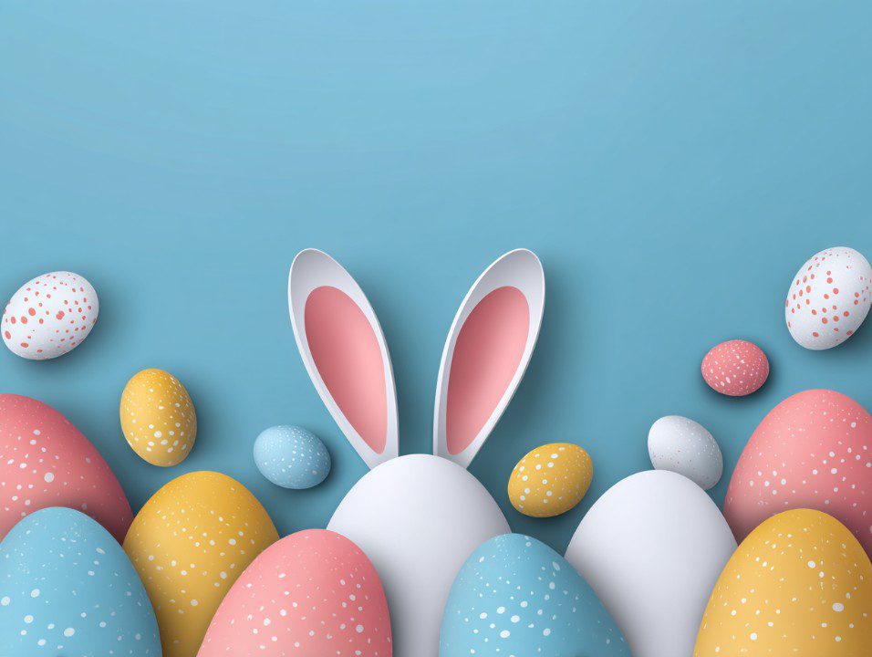 A playful Easter composition with white bunny ears and colorful speckled eggs arranged on a light blue background in pastel tones.