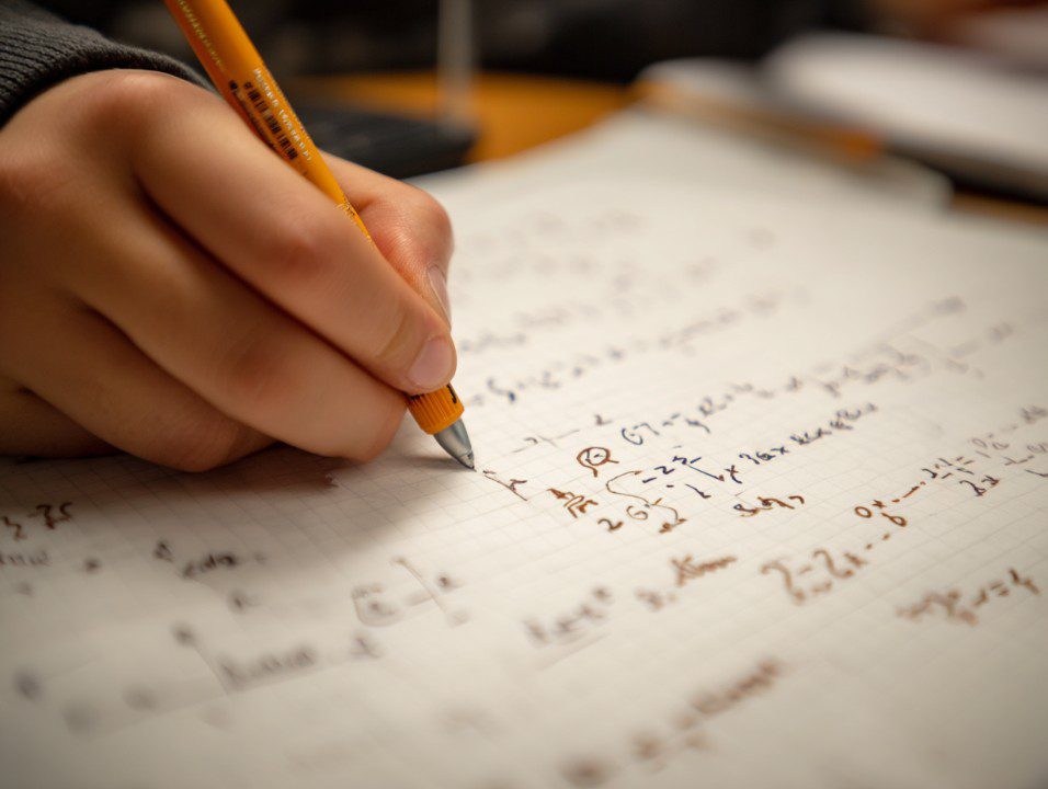 Close-up of a student's hand writing math equations on graph paper during a study or homework session, symbolizing focus and learning.