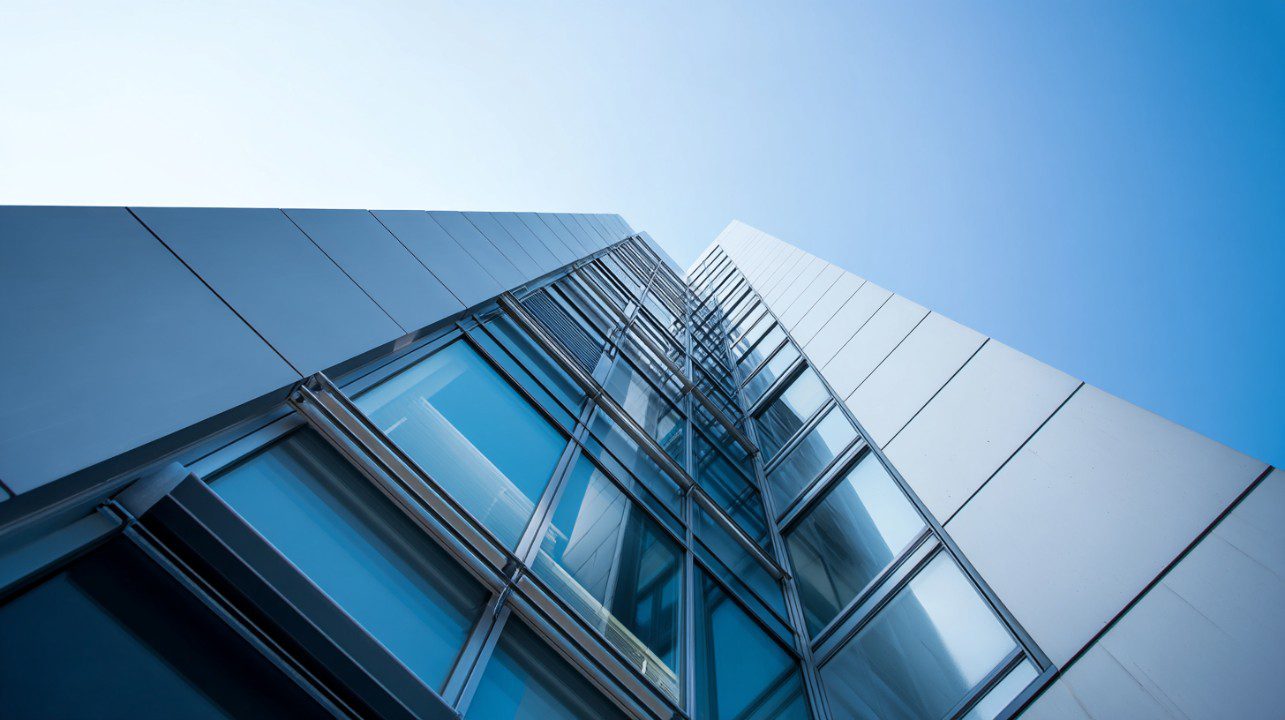 Low-angle view of a sleek modern skyscraper with reflective glass windows under a bright blue sky.