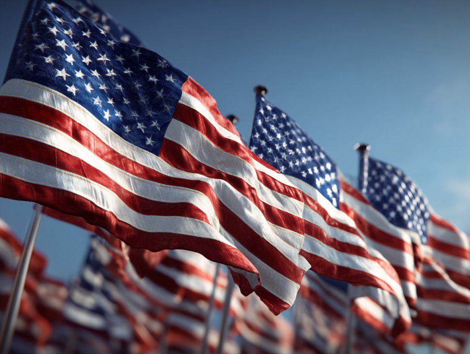 A row of American flags waving in unison against a blue sky, symbolizing unity, patriotism, and national pride.