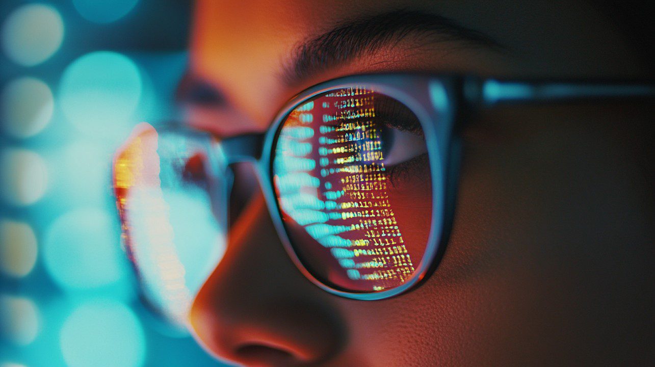 Close-up portrait of a person wearing glasses with colorful programming code reflected on the lenses, symbolizing digital innovation.