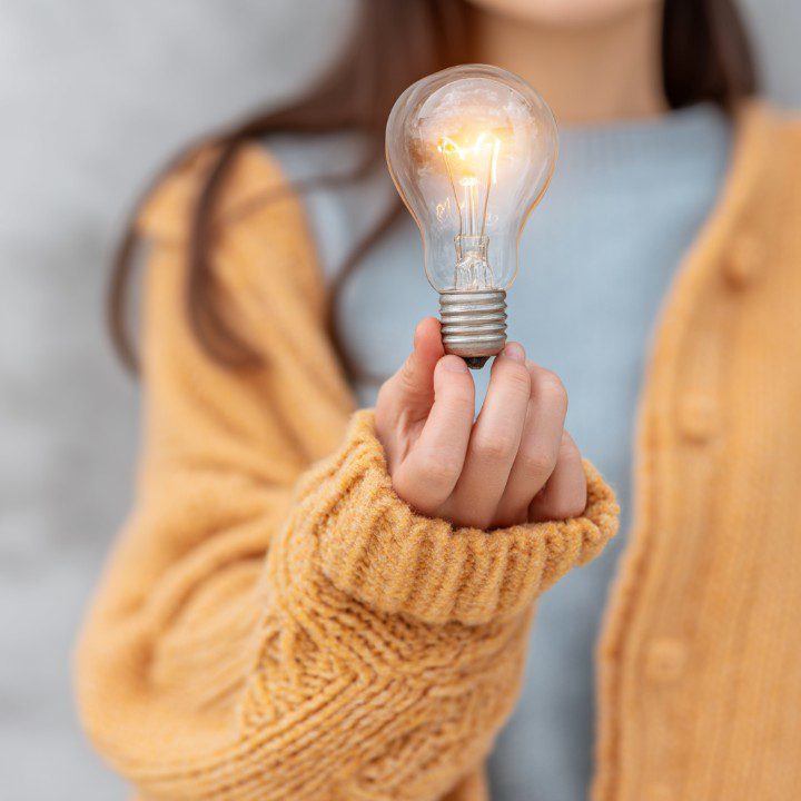 Close-up of a hand in a warm sweater holding a glowing light bulb, symbolizing a new idea and inspiration.
