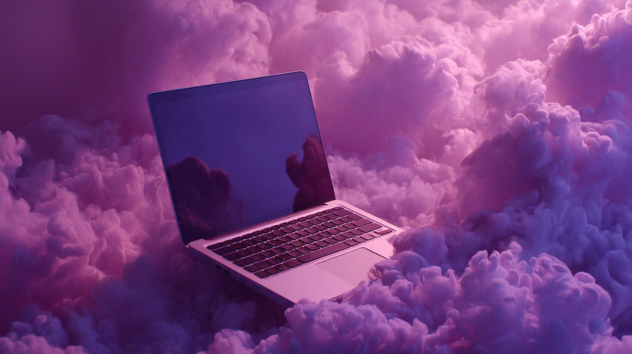 A laptop surrounded by fluffy purple clouds, symbolizing cloud computing, digital transformation, or tech creativity.