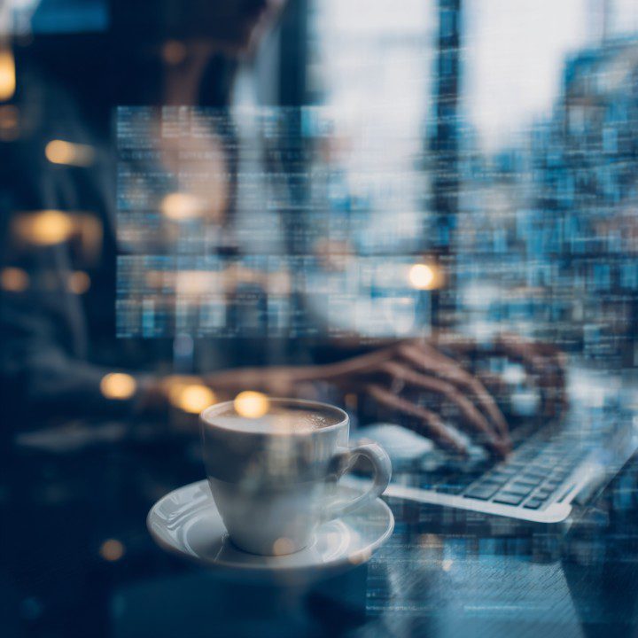 Abstract image of hands typing on a laptop with digital code overlays and a cup of coffee, representing cybersecurity and remote work.