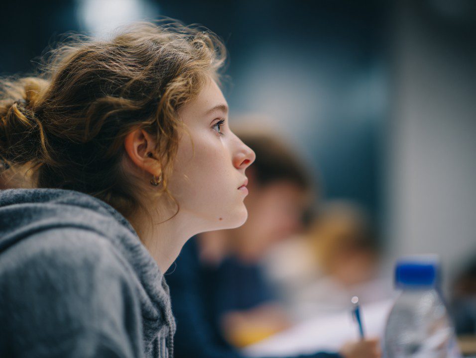 Side profile of a young female student attentively taking notes in class, symbolizing focus, learning, and academic engagement.