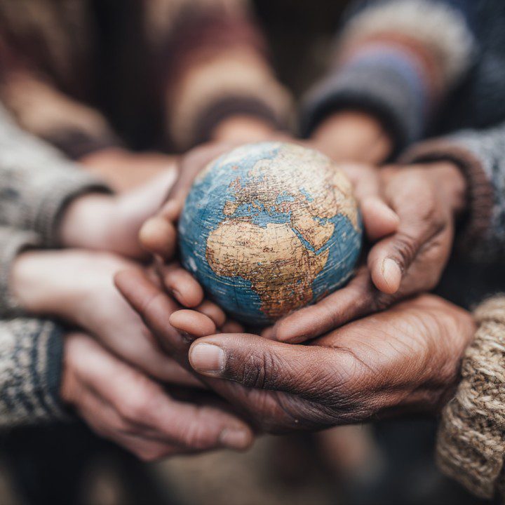 Multiple hands of different skin tones holding a globe, symbolizing unity, diversity, and shared responsibility for the planet.
