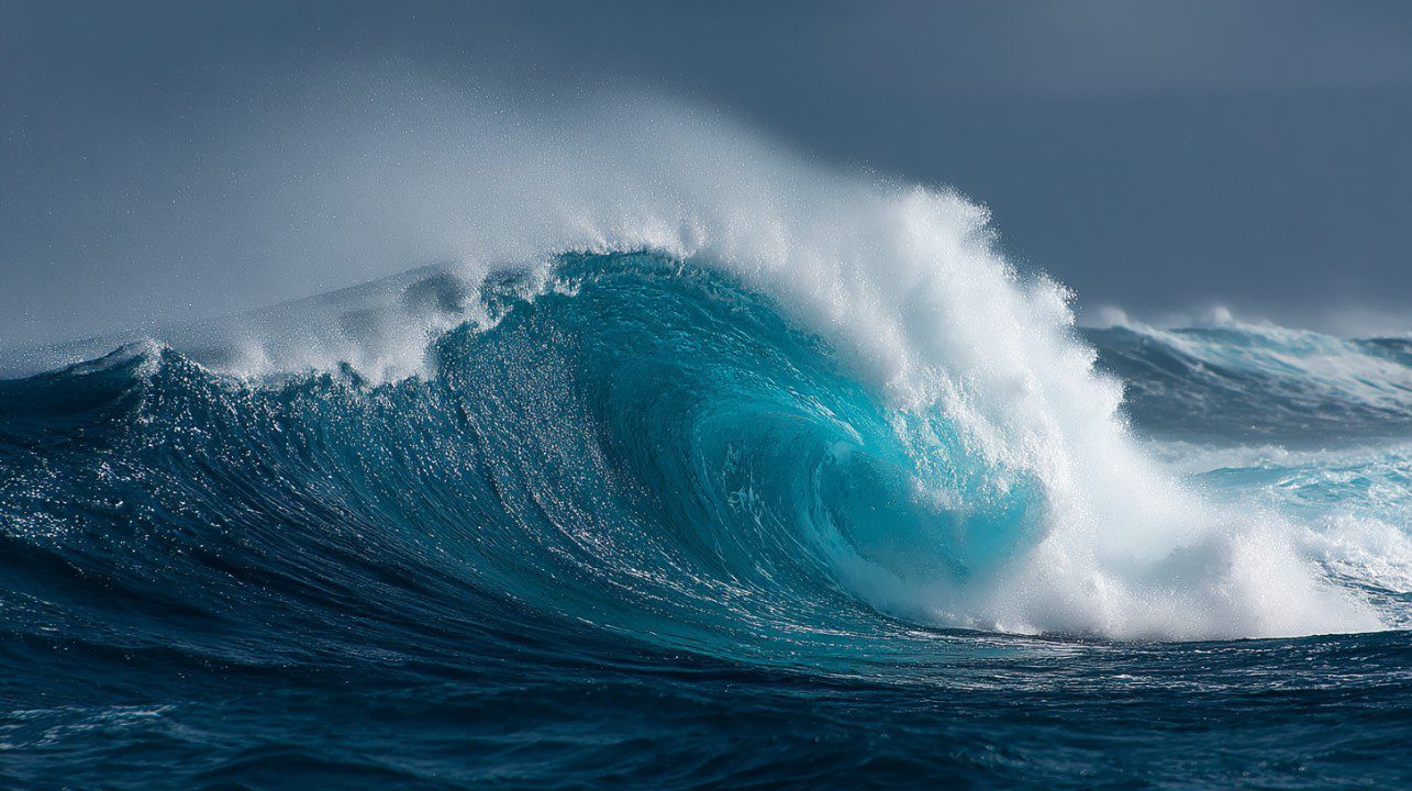 A powerful ocean wave curls and crashes in a dramatic display of motion and energy under moody skies.