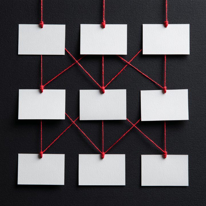 Blank white cards connected with red threads forming a network diagram against a black textured background.