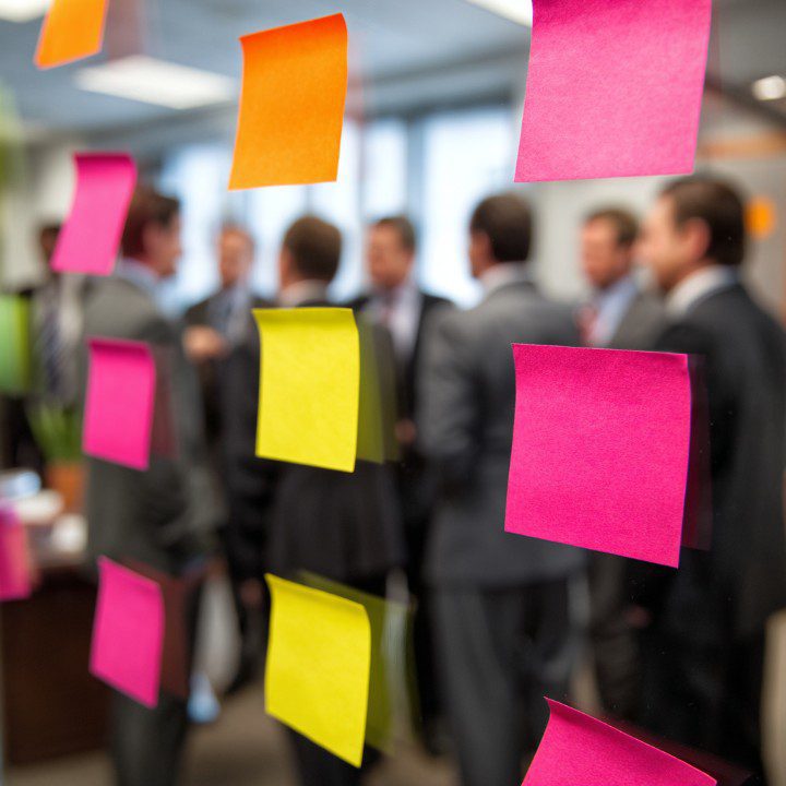 Business professionals in the background with colorful sticky notes on glass, illustrating teamwork and planning.