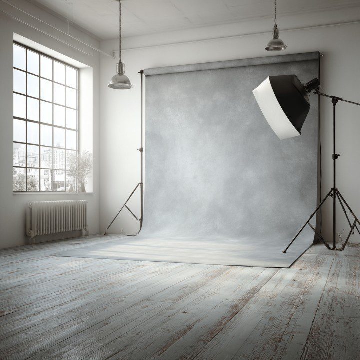 A modern minimalist photography studio featuring a soft light setup, gray backdrop, and natural window light in a bright room.