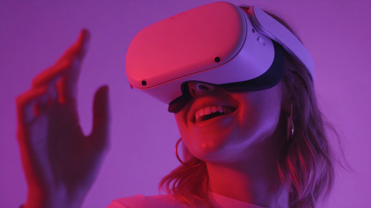 Smiling woman wearing a VR headset surrounded by pink and purple neon lighting, engaged in a virtual reality experience.