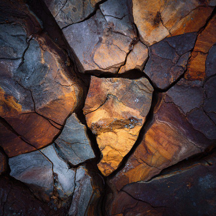 Close-up view of cracked and layered rock surface with rich earthy tones in brown, gray, and orange.