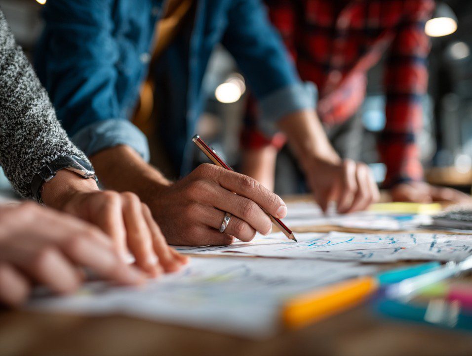 Close-up of a diverse group’s hands sketching ideas and plans on paper, illustrating teamwork and creative collaboration.