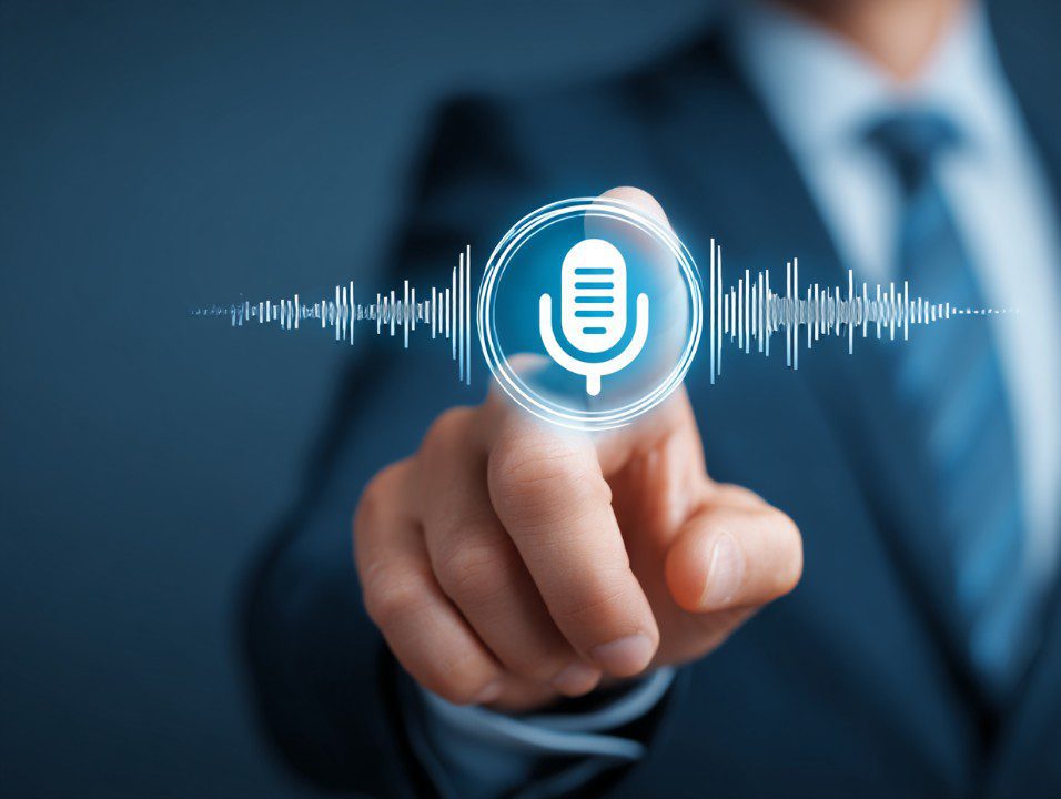 A businessman in a suit points at a glowing voice assistant icon, symbolizing smart technology and digital voice interaction.