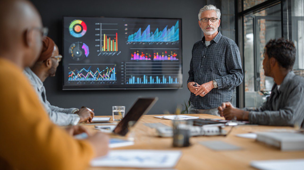 Mature businessman presenting big data analytics on a large screen during a meeting.