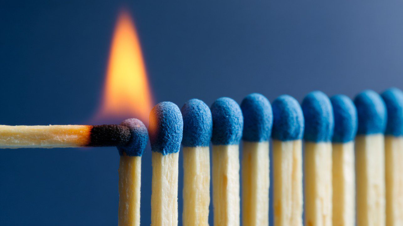 Close-up of a burning match igniting a row of blue-tipped matches.