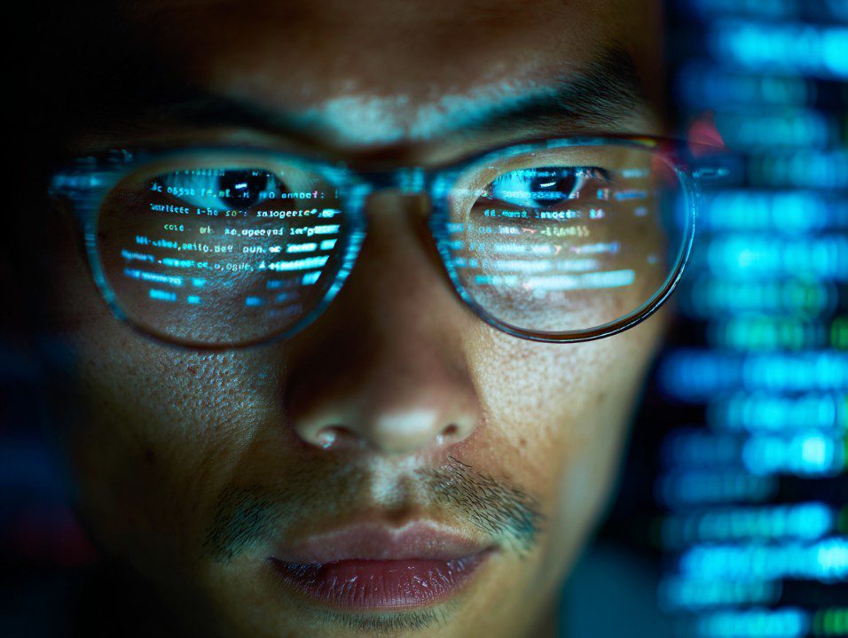 Close-up of a man with code reflected in his glasses, representing programming, cybersecurity, and tech innovation.