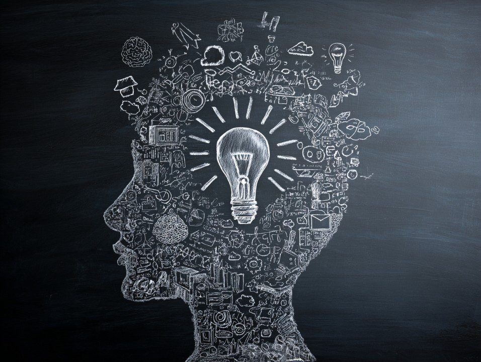 Chalkboard drawing of a human head silhouette filled with doodles and a central glowing light bulb.