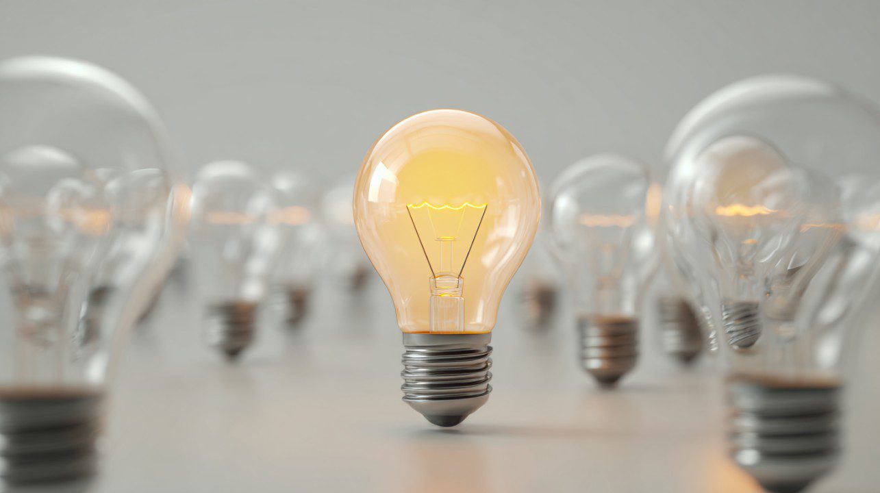 A single lit light bulb among several unlit bulbs representing innovation and creativity.