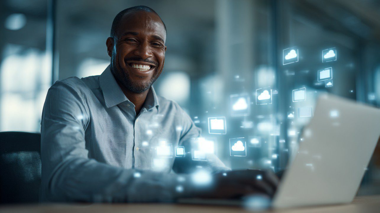 Confident African-American man smiling while working on a laptop with cloud and digital icons floating around, representing modern technology and cloud computing.
