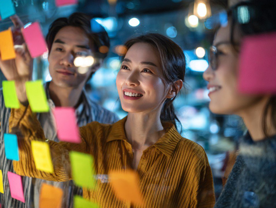 Group of creative professionals brainstorming ideas using colorful sticky notes on a glass wall in a collaborative modern office.